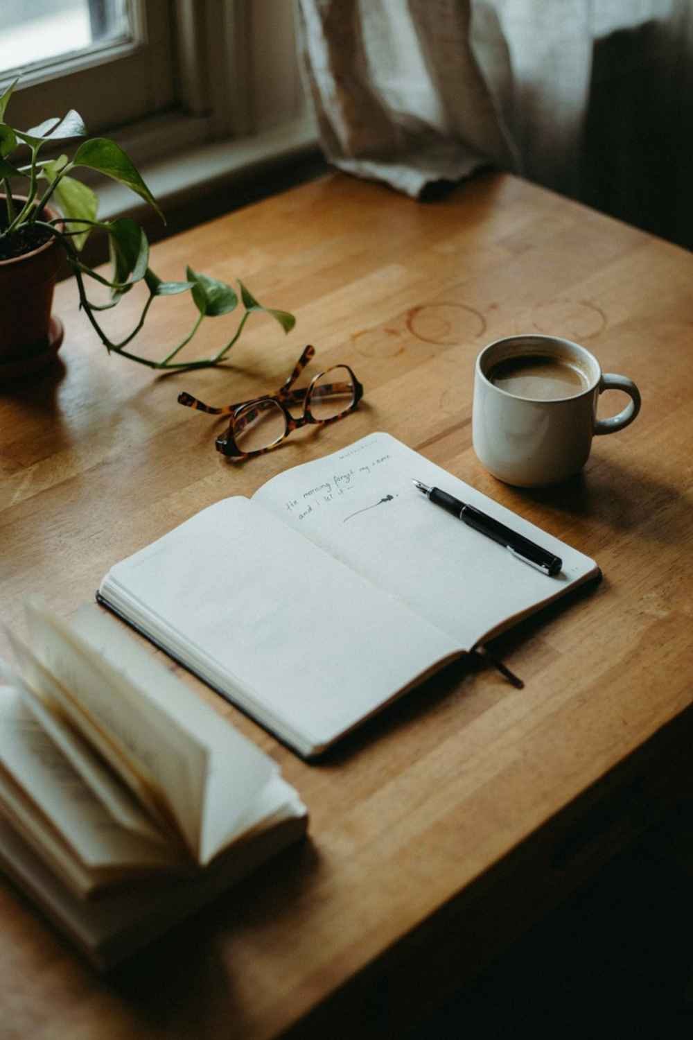 26 Overhead Morning Desk - 20 Cozy Prayer Corner Ideas for Small Bedrooms (Even a Studio Apartment) Overhead view of a wooden desk with coffee ring stains, glasses, an open journal and pen, and a potted plant